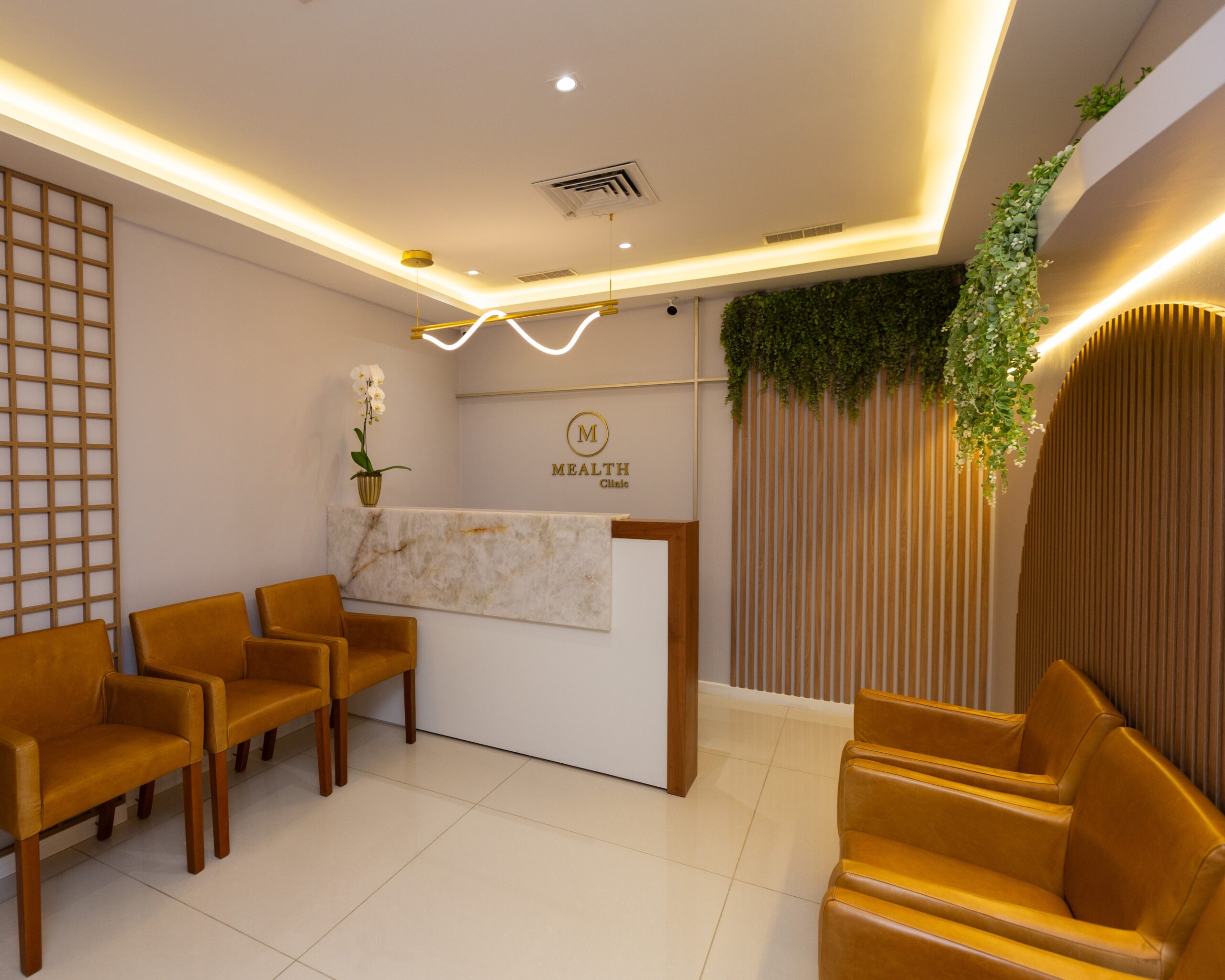 Sala de espera da clínica dermatológica, com foco em estética, localizada na Barra da Tijuca e no Cachambi. 3 poltronas de um lado e outras 3 do outro com o balcão no fundo. O ambiente é aconchegante e moderno.