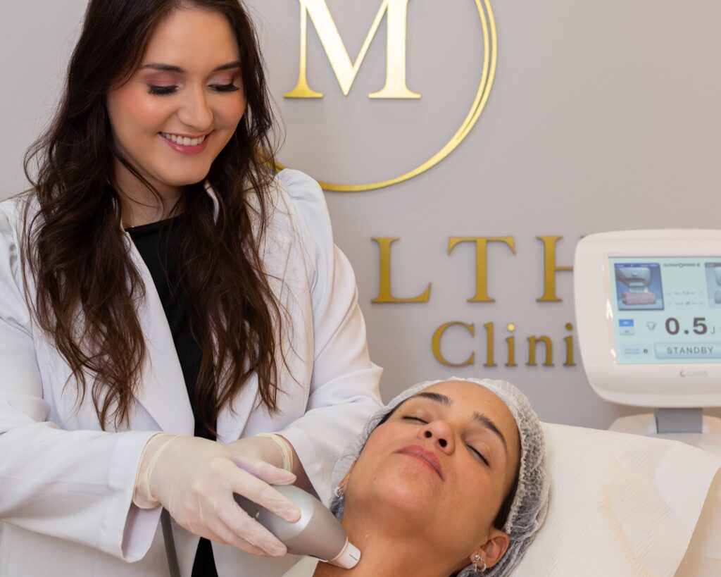 Dra Beatriz, dermatologista da Mealth Clinic, em pé operando ultraformer iii em sua paciente deitada na maca, na unidade da Barra da Tijuca, no Rj.