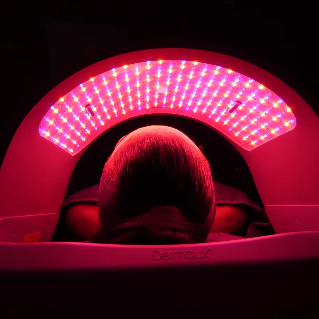 Pessoa deitada sob o painel do Dermalux Flex MD, LED médico no Rio de Janeiro, durante aplicação de fototerapia LED com luzes vermelhas e rosadas.