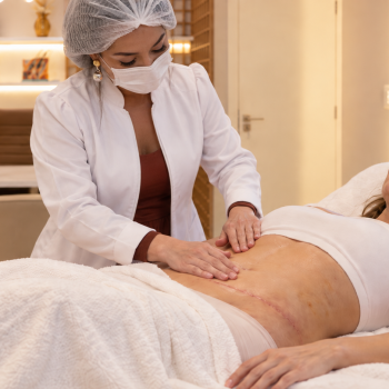 Profissional realizando avaliação e cuidados no pós-operatório de cirurgia plástica em paciente após abdominoplastia, com foco na recuperação, cicatriz e mobilidade dos tecidos.